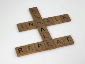 Wooden Scrabble tiles arranged to form the words 'Inhale, Exhale, Repeat' on a white background.